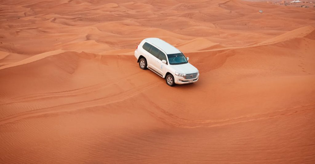 A white SUV drives through expansive sandy desert dunes, showcasing offroad adventure.