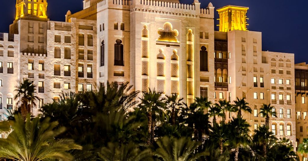 A stunning night view of a luxurious hotel with palm trees reflecting on water in Dubai.