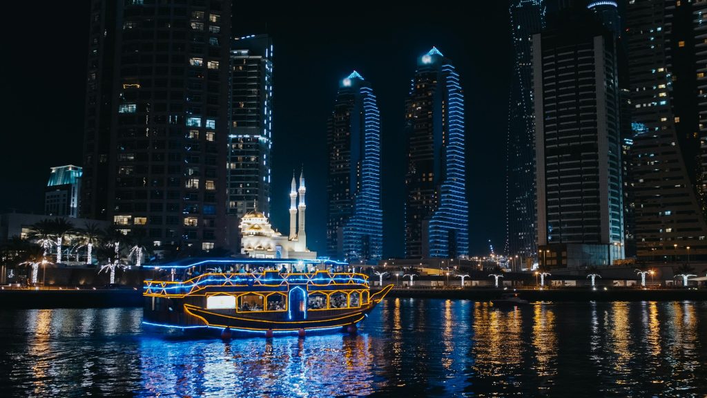 Stunning Dubai marina skyline at night with illuminated buildings and cruise boat on the water.